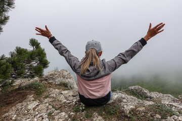 A picturesque mountain landscape in the clouds on Ai-Petri mountain in the Crimea. A woman on the background of a high-altitude landscape with trees in the clouds. Fog on the mountain.