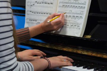 Human hands of a piano teacher explaining to a student playing the keys notes and chords on a...