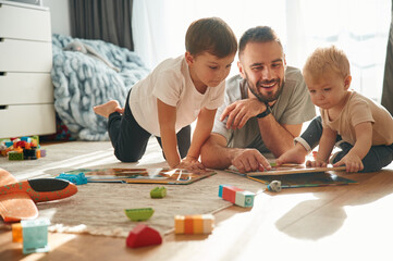 Lying down, board game. Father is playing with two little boys on the floor with toys