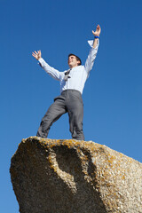 Businessman, success and freedom on cliff with sky, rock and peak of mountain in nature. Happy, person and celebration of winning an achievement, challenge or climbing in business and career progress