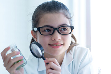 Cute student girl in a lab coat uses a magnifying glass and holding glass bottle from tissue...