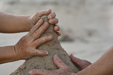 Close-up Senior couple's hand playing together in the sand on a tropical beach, Building a sand castle