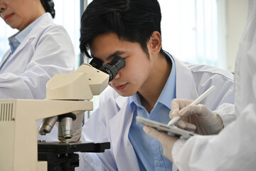 Asian male scientist working with the microscope, analyzing biochemical samples in the science...