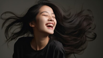 Fototapeta premium A Asian woman joyfully laughs and smiles, seated on a gray studio background.