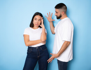 Portrait of a upset young couple having an argument and gesturing over blue wall