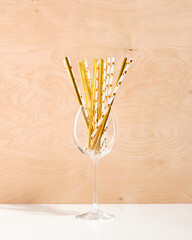 A champagne and wine glass stands on a white table with lots of straws gold color for cocktails and other alcoholic drinks.