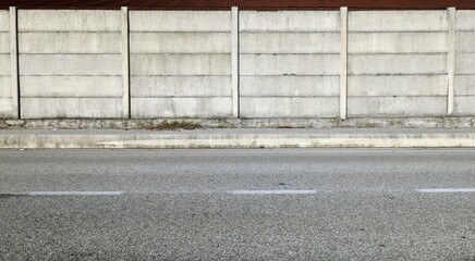 Grunge concrete precast compound wall at the road side with cement sidewalk and road in front....