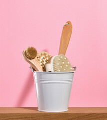Fototapeta na wymiar White metal bucket with eco friendly wooden supplies for skincare procedures on a pink background.