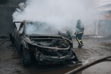 Firefighters extinguish a burning car on the street. Burnt car. Rescuers. Strong smoke. Emergency....