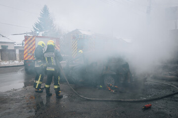 Firefighters extinguish a burning car on the street. Burnt car. Rescuers. Strong smoke. Emergency....