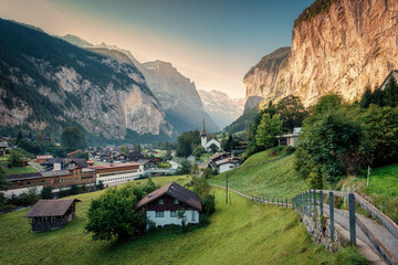 View of Lauterbrunnen valley with rustic village, famous church and Staubbach falls during end of summer at Switzerland - obrazy, fototapety, plakaty