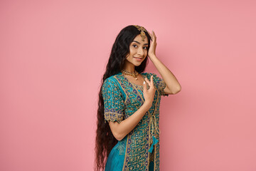 jolly young indian woman in national costume posing with hand near face and smiling at camera
