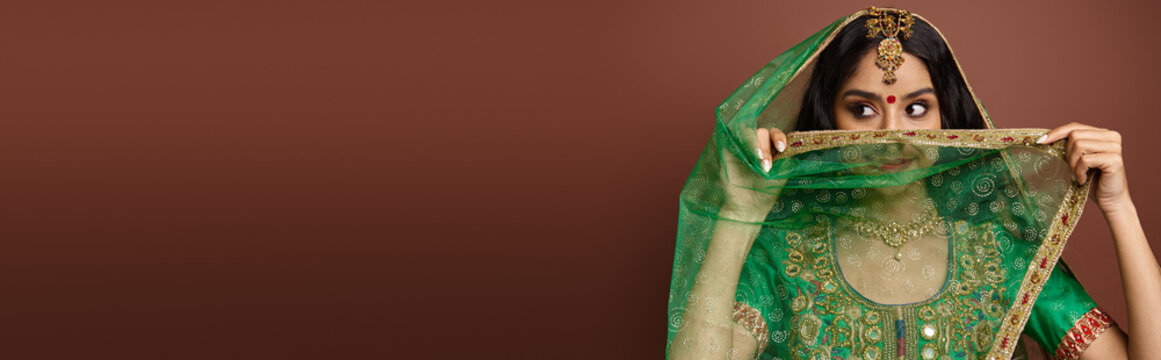 pretty indian woman with bindi dot on forehead covering face with green veil looking away, banner