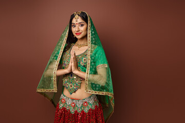 pretty jolly indian woman with bindi and green veil showing praying gesture and smiling at camera