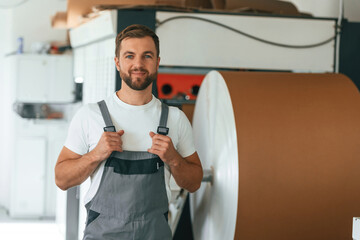 By the rounded machine for making paper. Handsome man is working at the factory of creating eco boxes