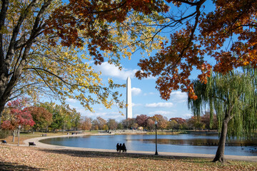 Washington monument and its reflection in DC framed by fall colors and skies with puffy clouds on a...