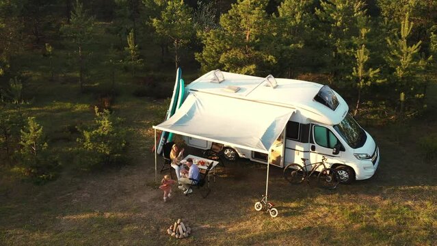 A family of three sitting at a table outside a motorhome in the woods . Travel concept
