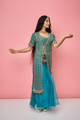 attractive woman in traditional clothing with accessories posing with open palms on pink backdrop