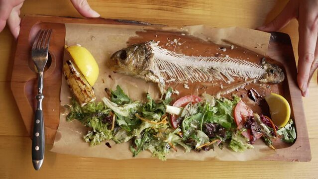 A fish skeleton and the remains of a salad lie on a wooden plate