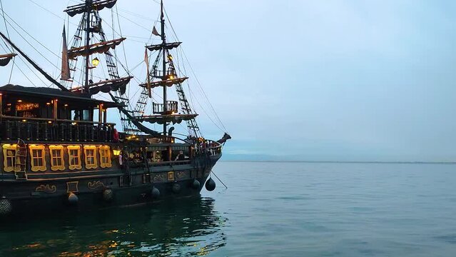 Old dark pirate ship with masts and weathered sails, sailing the sea with waves and the sky with clouds. Scene for an epic adventure and treasure story.