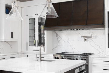 A kitchen detail with white cabinets, a brown metal range hood, white marble countertops and...