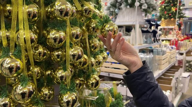 A person's hand touching golden Christmas baubles on a decorated tree at a festive holiday store