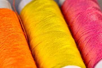 Spools of orange, yellow and pink thread for sewing. Spools of colored threads