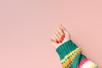 Female hands with red manicure and striped sweater against pink background.