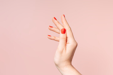 Female hand with red manicure against pink background.