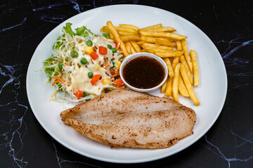 Steak grilled fish topped with black pepper sauce with french fries and vegetable salad put in dish on black marble background. Meat steak and french fries serving plate fast food meal. Steak meal set