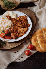 on a plate there is a dish with rice and several pieces of grilled meat. Decorated with vegetables and herbs. Fresh loaf of bread, fresh vegetables