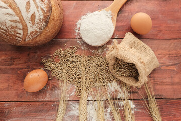 Ears of wheat, bag of grain on a wooden background. Round whole grain bread, flour - ingredients...