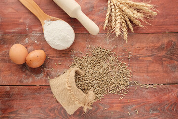 Ears of wheat, bag of grain on a wooden background. Rolling pin, eggs, flour - ingredients for...