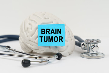 On a white surface next to the stethoscope lies a brain on which a sticker with the inscription - Brain tumor