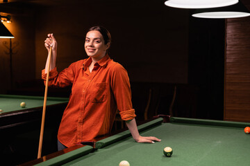 Young professional woman playing billiards in the dark billiard club