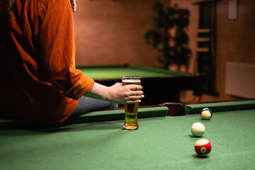 Woman playing American billiards sitting on a pool table with a glass of beer