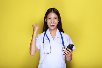 Portrait of a beautiful young woman in a yellow background, Asian woman poses with a cell phone while wearing a doctor's uniform and a stethoscope.