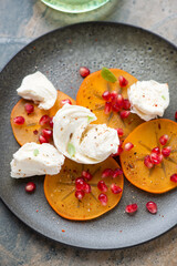 Obraz premium Olive-colored plate with persimmon slices, torn mozzarella and pomegranate seeds, vertical shot, middle closeup