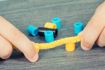 Preschooler hands with creative sticks and beads used to making bracelets. Development of kids motor skills, coordination and logical thinking