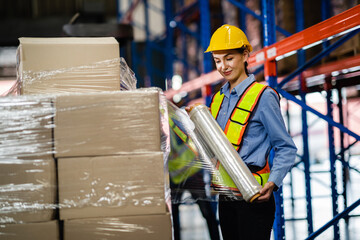 Warehouse workers wrap parcels in stretch film on pallets in a factory warehouse. Wrapping boxes...