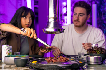 close-up of a couple in love at a table having lunch in a Korean restaurant picking juicy meat from the grill with tongs
