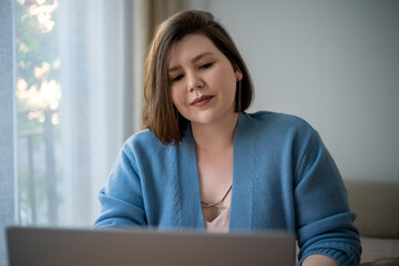 Young brunette plus size woman using laptop at home.
