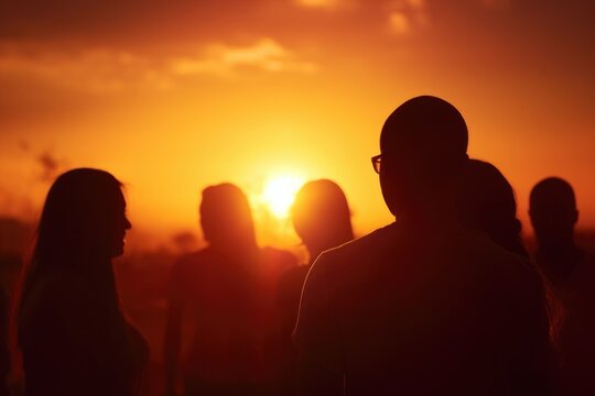 A group of people standing together, gazing at the beautiful sunset. This image can be used to depict friendship, unity, or the beauty of nature