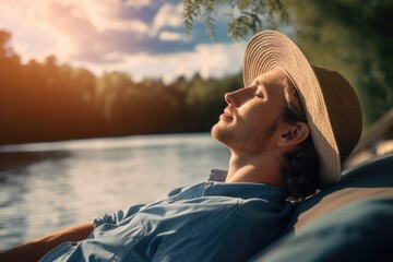 A man wearing a hat is seen relaxing by the water. This image can be used to depict leisure, vacation, or peaceful moments near a body of water