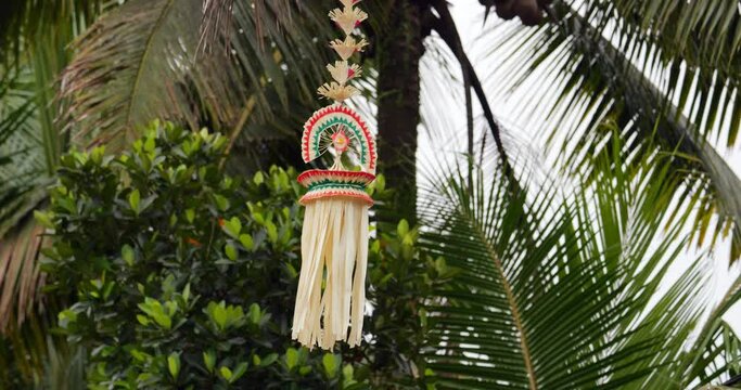 Hand-made decoration hanging at rope on end of penjor pole, wisp from leaves move on wind. This part of traditional decoration installed at Balinese village street is called Sampian penjor