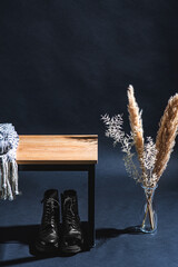 interior and home decor concept - close up of blanket on bench, lace-up boots and dry plants in vase in dark room