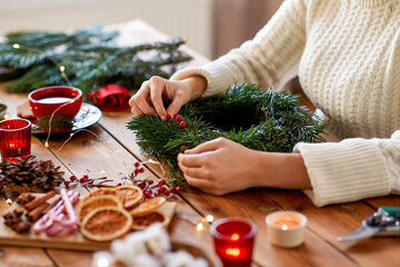 winter holidays, diy and hobby concept - close up of woman with berry decorations making fir...