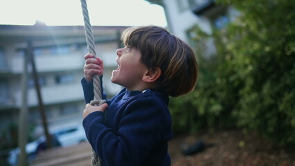 Heartwarming Close-Up of Joyful Child Sliding on Wire Rope Between Trees, Nostalgic Park Fun. Young boy holding tight and sliding down
