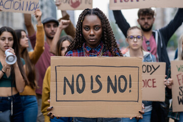 Young woman firmly holding a 'No Is No' sign, symbolizing empowerment at a feminist rally - obrazy, fototapety, plakaty