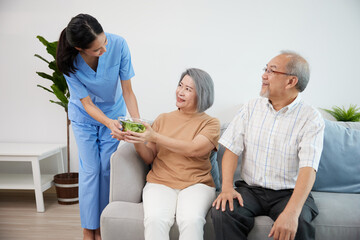 nurse or caregiver serving vegetables in a bowl to senior couple on sofa